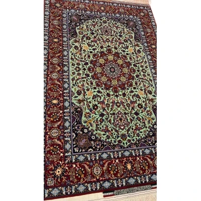 "Detailed view of a luxurious Seirafian Persian rug with silk and wool, featuring vibrant floral patterns on a light green background, hand-knotted in Isfahan."